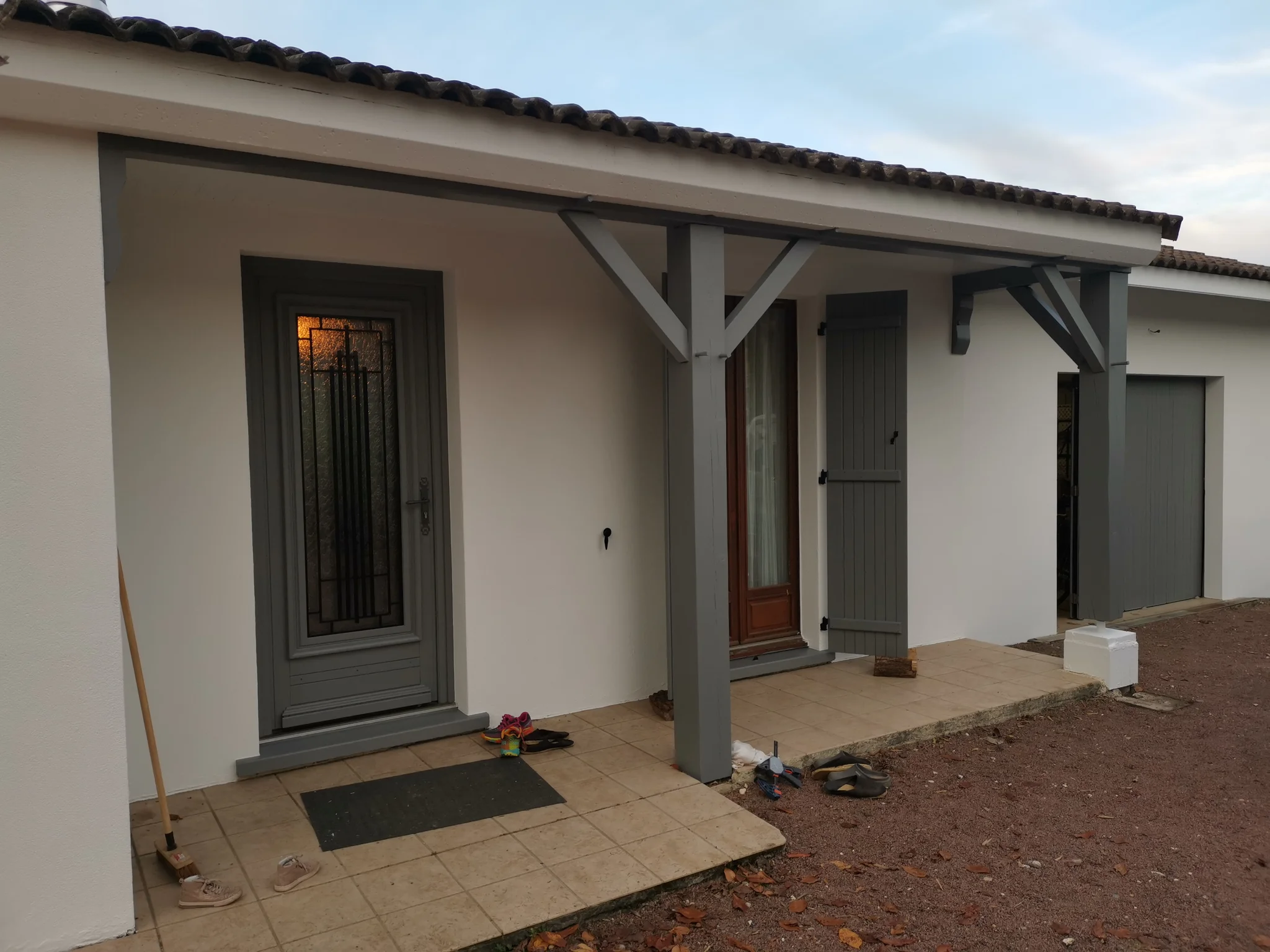 Entrée de maison après travaux : façade blanche, porte, volets et poteaux peints en gris